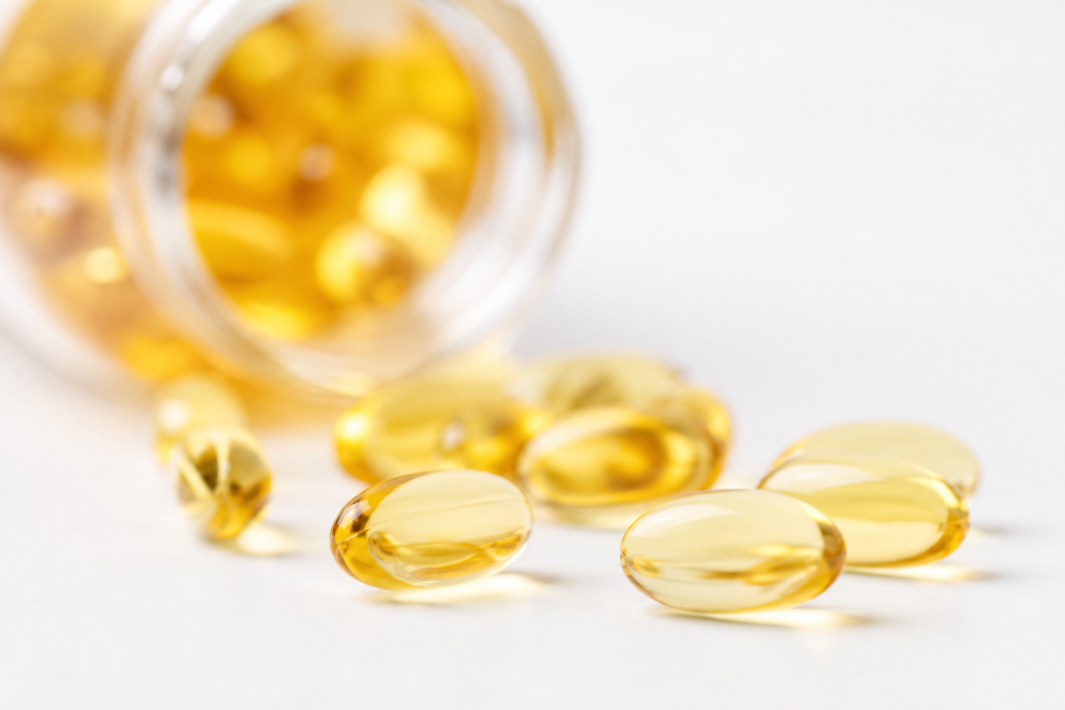 Close-up of omega-3 fish oil capsules on white background, bottle in background.